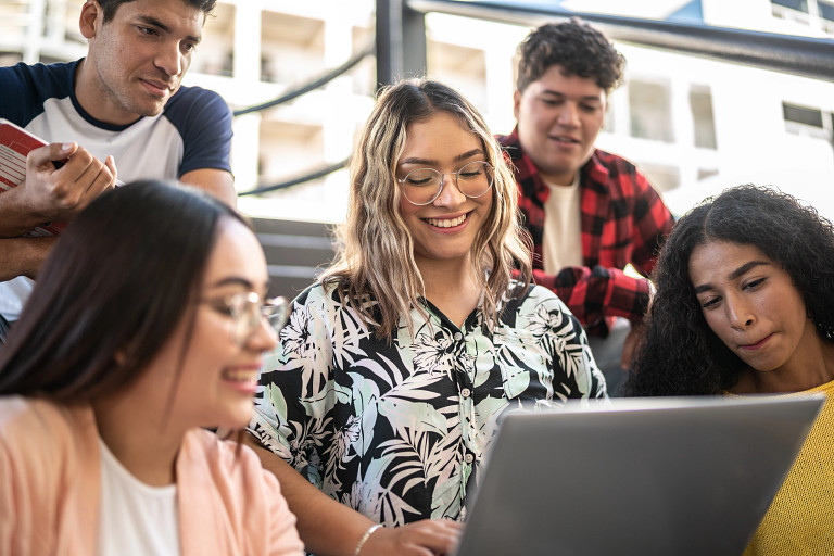 A group of smiling students gathering around a laptop